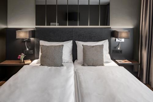 a bedroom with two beds with pillows and two lamps at Hotel AMANO Düsseldorf in Düsseldorf