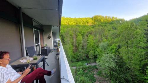 a man sitting on a balcony looking out at the forest at Urlaub mit Sauna und Pool ist cool! in Bad Harzburg