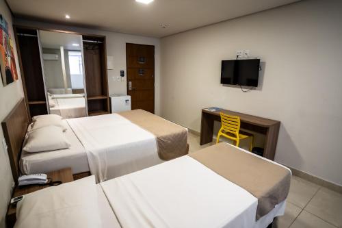 a room with three beds and a desk and a tv at Bessa Beach Hotel in João Pessoa