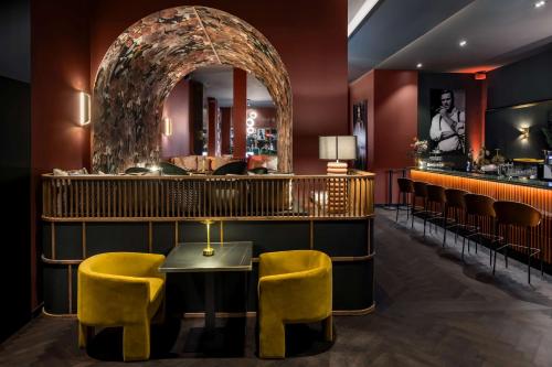 a bar with yellow chairs and a table and a mirror at Hotel AMANO Düsseldorf in Düsseldorf
