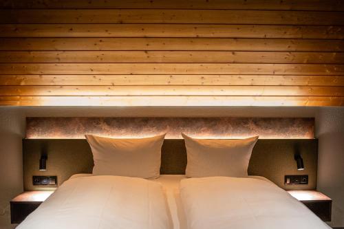 a bed with a wooden headboard with two white pillows at Hotel Hofgut Sternen - Ravennaschlucht in Breitnau