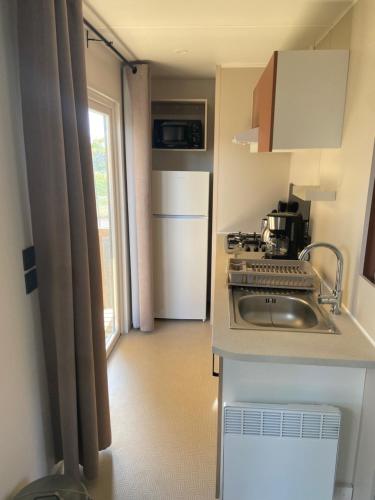 une petite cuisine avec un évier et un réfrigérateur dans l'établissement mobil-home 3 chambres calme et tout équipé à carry-le-rouet proche piscine avec toboggans pataugeoire et animations peu de vis à vis terrasse barbecue paddle bodyboards accès libre aux activités du camping lou soulei commerces et plage à proximité, à Carry-le-Rouet