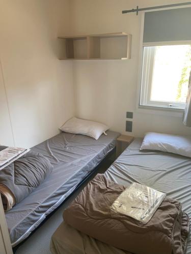 deux lits dans une petite pièce avec une fenêtre dans l'établissement mobil-home 3 chambres calme et tout équipé à carry-le-rouet proche piscine avec toboggans pataugeoire et animations peu de vis à vis terrasse barbecue paddle bodyboards accès libre aux activités du camping lou soulei commerces et plage à proximité, à Carry-le-Rouet