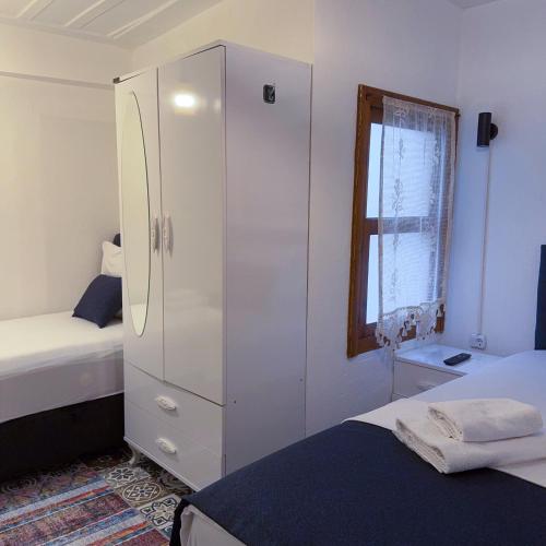 a bedroom with a white cabinet and a bed and a window at Hera Pansiyon in Ayvalık