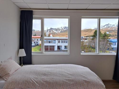 a bedroom with a bed and three windows with mountains at The Old Post Office Guesthouse in Grundarfjordur