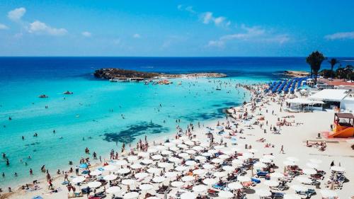 a crowd of people on a beach with umbrellas at Cornelia Hotel Ayia Napa Center in Ayia Napa