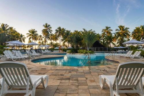 a resort pool with white chairs and palm trees at Costa do Sauípe Resorts in Mata de Sao Joao