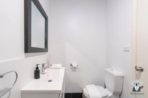 a white bathroom with a toilet and a sink at KozyGuru | Balmain | Charming 3 Room cottage in Sydney