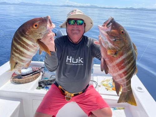 a man holding two fish on a boat at Hotel Huacas in Huacas