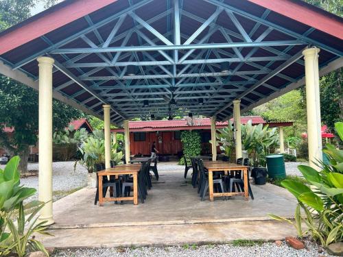 a patio with wooden tables and chairs under a roof at Capital O 91152 Jerot Dusun Campsite in Kampong Bukit Tumboh