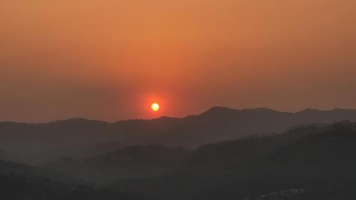 a sunset over a mountain range with the sun in the sky at Mahi Restaurant & Guest House in Almora