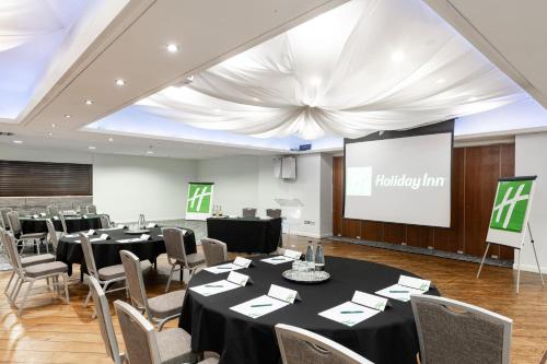 a conference room with tables and chairs and a screen at Holiday Inn - Manchester - Oldham by IHG in Manchester