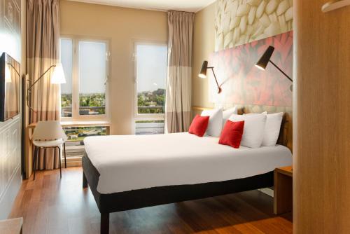 a hotel room with a large white bed with red pillows at Ibis Casablanca Sidi Maarouf in Casablanca