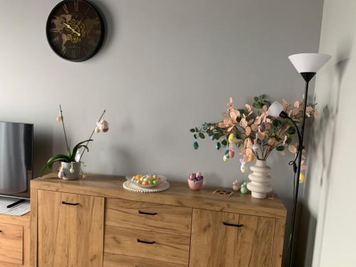 a wooden cabinet with flowers and a clock on the wall at Bulwar Apartament Stare Miasto in Głogów