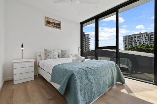 a white bedroom with a bed and a large window at Cozy 1BR Retreat in Hamilton Near River and Dining in Brisbane