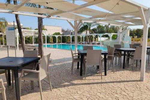 un grupo de mesas y sillas bajo un pabellón junto a una piscina en OWNER ITALY Residence, en Torre Lapillo