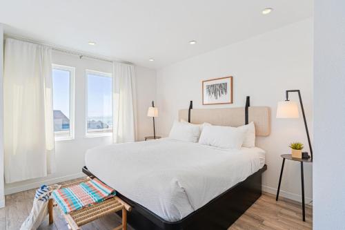 a bedroom with a bed with white sheets and two windows at 2 Coastal Studios at Cayucus Beach Access Ocean Views in Cayucos
