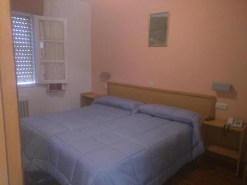 a bedroom with a bed with blue sheets and a window at Restaurante y Hostal San Paio in Santiago de Compostela