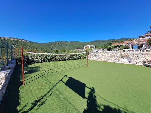 a tennis court with a net on a green field at Villa Stone House Poplat in Vela Luka