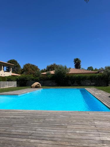 une grande piscine bleue avec une terrasse en bois dans l'établissement Les Jardins d’Alzetu, à Porto-Vecchio