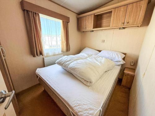 a small bedroom with a bed with white sheets and a window at Brilliant 6 Berth Caravan For Hire With Decking By The Norfolk Coast Ref 50064G in Great Yarmouth