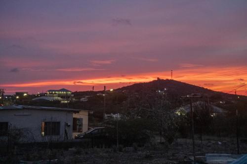a sunset over a hill with a house and a mountain at Kunukuhuis Hofi Abundansia in Willemstad