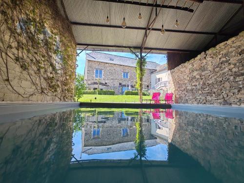 a pool of water with pink chairs and a building at La Source Du Bonheur Chambres et Table d'Hôtes in Rieupeyroux