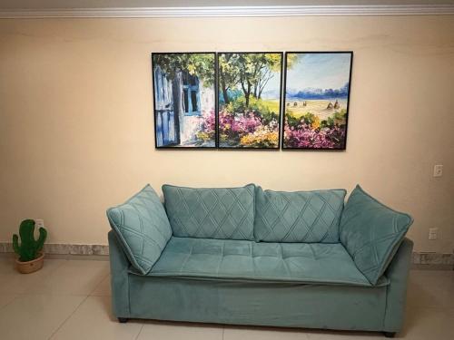 a blue couch in a living room with three paintings on the wall at Casa com piscina in São Pedro da Aldeia