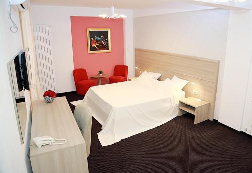 una habitación de hotel con una cama blanca y sillas rojas en Parliament Square, en Bucarest