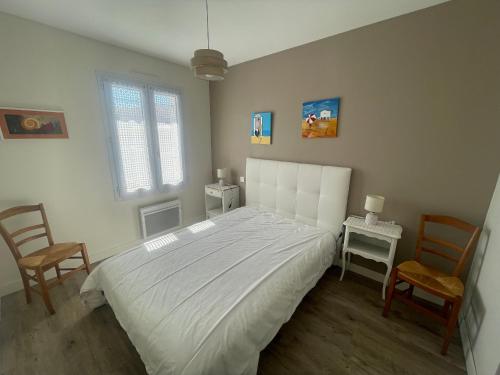 une chambre avec un grand lit blanc et deux chaises dans l'établissement Charmant T3 proche plage, terrasse et jardin clos, quartier calme. - FR-1-92-879, à Les Sables-dʼOlonne