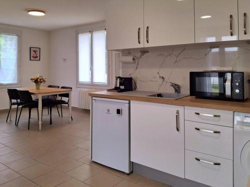 une cuisine avec des armoires blanches et une table avec un micro-ondes dans l'établissement À 300 m de la plage, charme et tranquillité à Merville-Franceville - FR-1-788-66, à Merville-Franceville-Plage