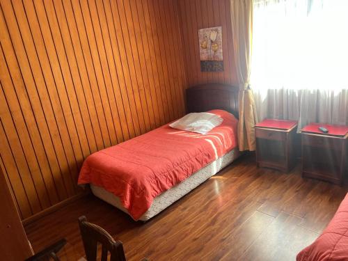 a bedroom with a small bed with a red blanket at Hotel Plaza Los Leones in Curanilahue