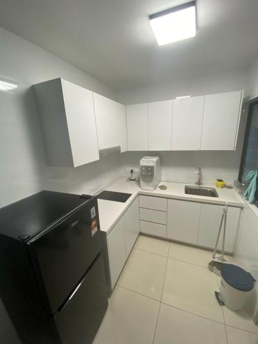 a kitchen with a black refrigerator and white cabinets at Tulip Residence Elmina in Shah Alam
