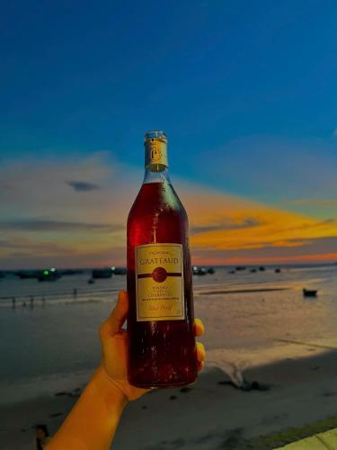 a person holding a bottle of alcohol on the beach at Lê Huỳnh Guest House Family in Ke Ga