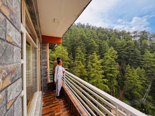 two people standing on a balcony looking out at the forest at Staynest BNB in city Centre - 3 BHK apartments - PRIVATE PARKING - BALCONY VIEW in Shimla