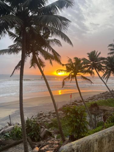 a sunset on the beach with palm trees at SEVENSTAR RESIDENCY in Varkala