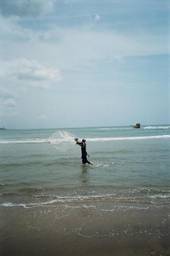 a man standing in the ocean with a net at Adinam's Beach Retreat in Nyanyanu