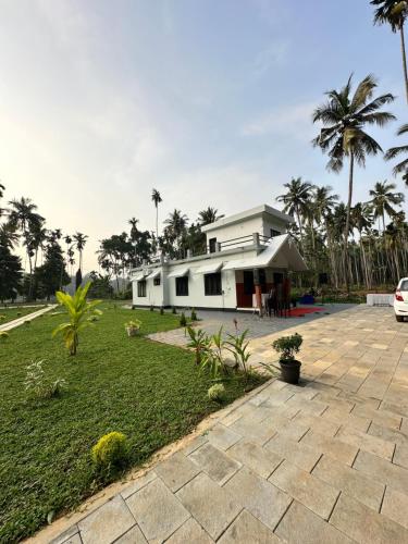 a white house with palm trees in the background at Natures Adobe in Nilambūr