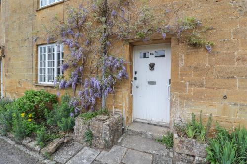a brick house with a white door and purple flowers at Two Towers Cottage in Montacute