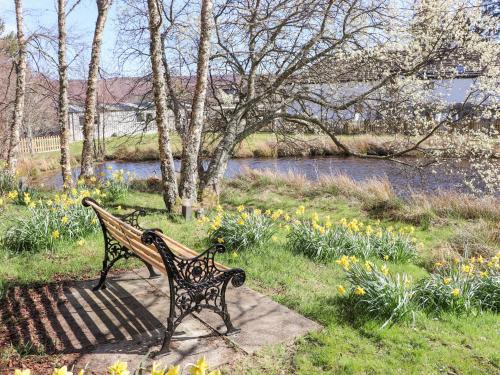 a park bench sitting next to a river with flowers at Larch in Newtonmore