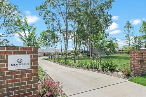 a path in a park with a brick wall and a sign at Mala Retreat Sleeps 7, Two Bedrooms & Ensuites in East Maitland