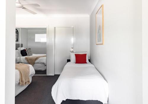 a white bedroom with a bed with a red pillow at Mala Retreat, Shiraz Suite 5 Star Immaculate and Comfortable in East Maitland