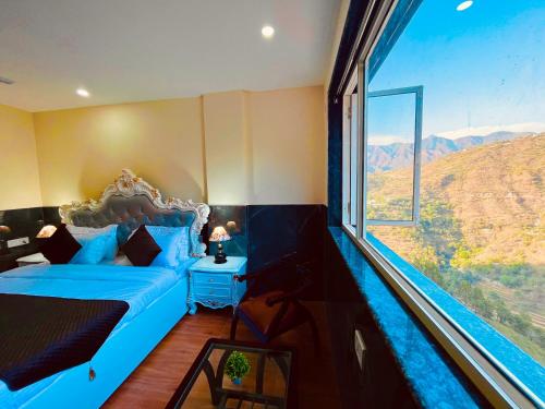 a bedroom with a blue bed and a large window at River Grand Resort - A Peaceful Stay Kempty Fall Mussoorie by Sitara Group in Mussoorie