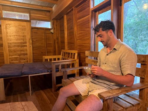 un uomo seduto su una panchina con una tazza di caffè di Attale eco resort a Nikawatawana