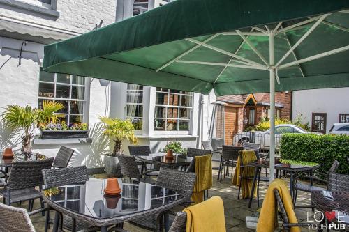 een patio met tafels en stoelen en een grote groene parasol bij The Robin Hood Inn in Rowlands Castle