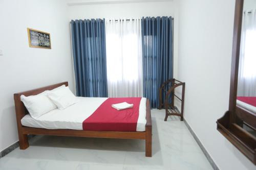 アヌラーダプラにあるHiru Holiday Homeのベッドルーム1室(赤毛布と青いカーテンのベッド1台付)