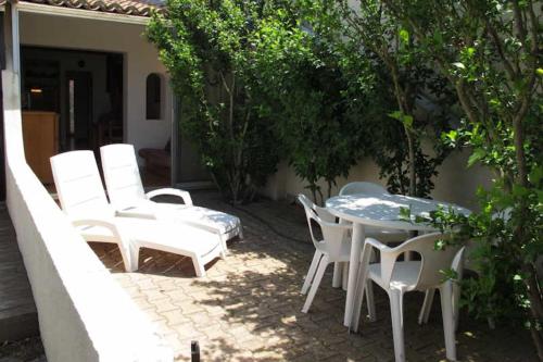 une terrasse avec des chaises blanches, une table, une table et des chaises dans l'établissement Naturiste Cap d'Agde Villa Héliovillage 10, au Cap d'Agde