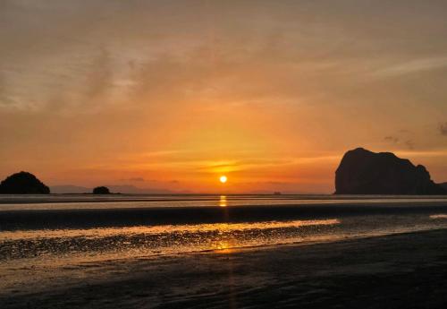 a sunset on the beach with rocks in the background at The Nanda Beach Resort in Sikao