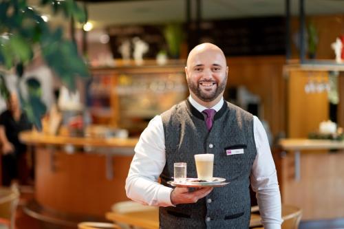 a man holding a tray with a cup of coffee at Vivea Gesundheitshotel Bad Häring in Bad Häring