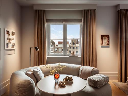 a living room with a couch and a table and a window at Rosewood Amsterdam in Amsterdam
